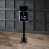 Capture Your Spin A stylish Eclipse - DSLR Flash Photo Booth (Black) with a touchscreen display is situated in a room featuring gray paneled walls and wooden flooring.
