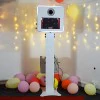 Capture Your Spin A 15.6” LG Touch Screen Selfie Mirror Photo Booth in white is surrounded by colorful balloons and string lights in a lively room.